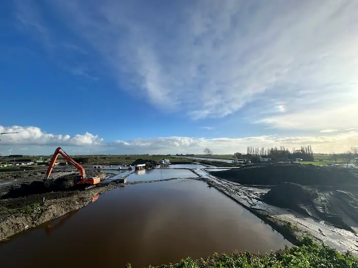 Grond- en slibbank van Groba Groep in Harlingen met baggerdepots, waterbassins en een graafmachine in werking voor verwerking en ontwatering van slib.