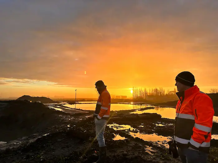 Medewerkers op de slib- en grondbank bij zonsopkomst, vroeg aan het werk met baggerverwerking.