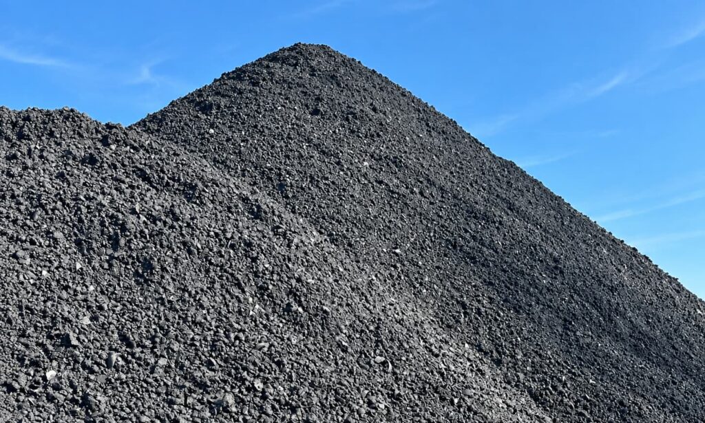 Large mound of black coal against a clear blue sky, showing rough, chunky texture and a steep slope.